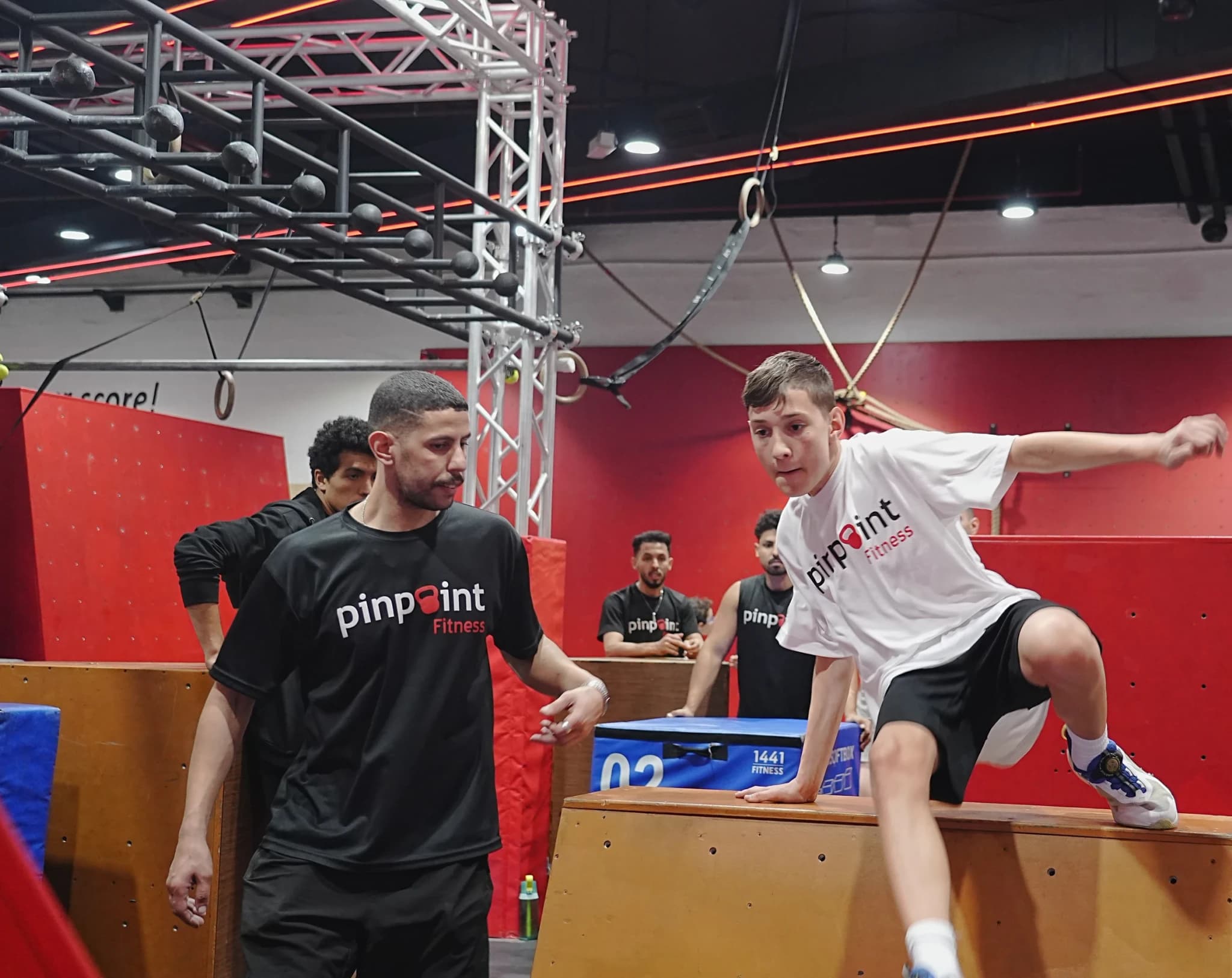 A boy vaulting over a box at Pinpoint Fitness as his coach looks on