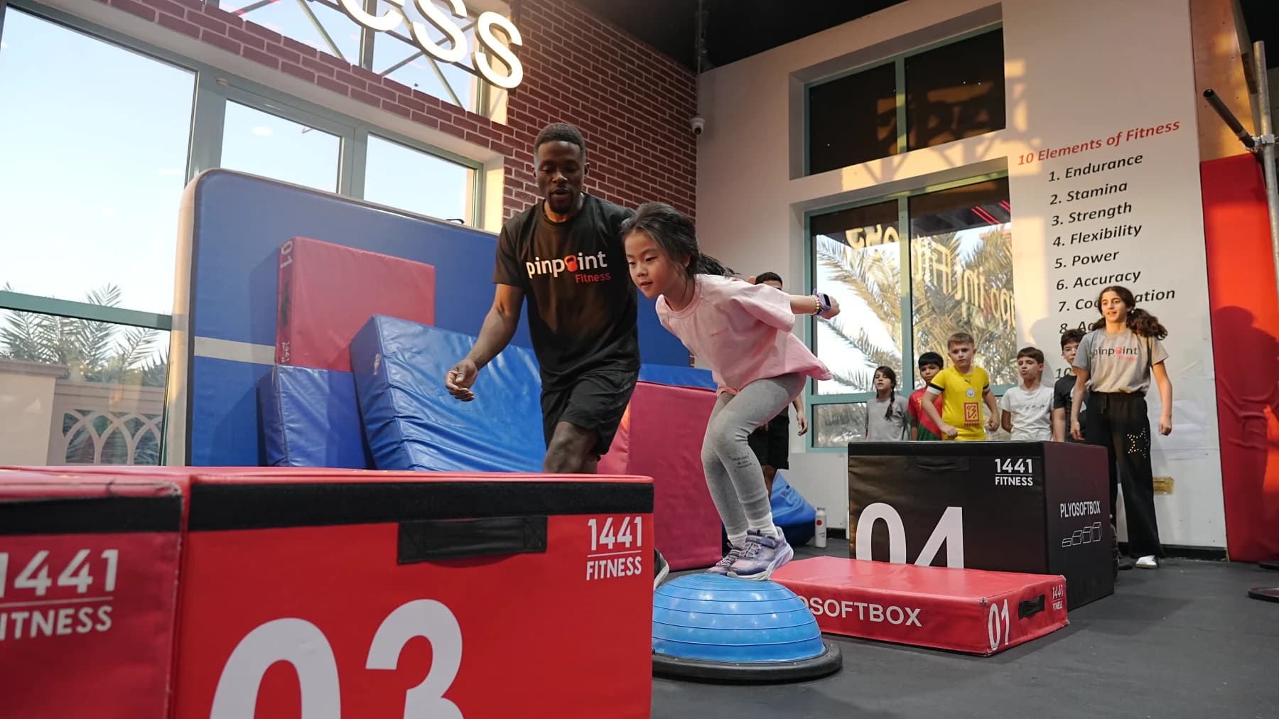 A coach helping a child jump onto an obstacle box at Pinpoint Fitness